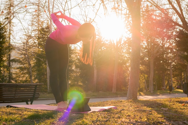 Mulher faz exercícios de ioga em um parque ao pôr do sol