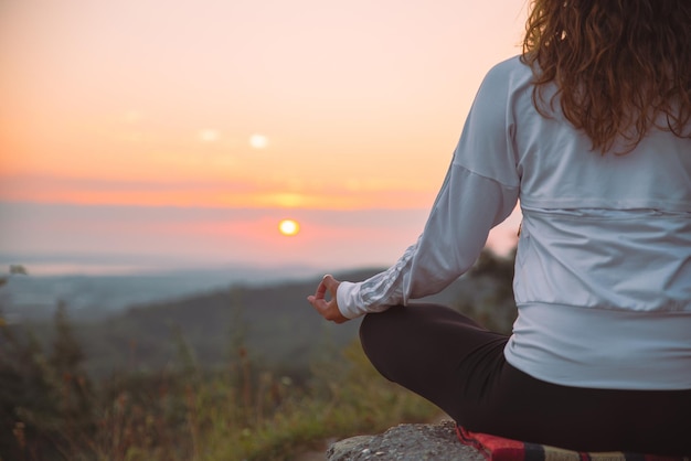 Mulher faz exercícios de ioga no topo da colina ao nascer do sol