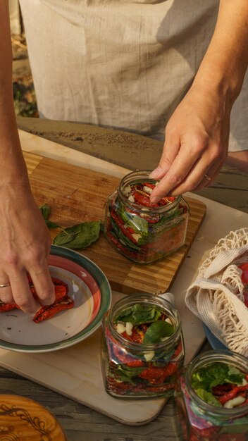 mulher faz preparativos para tomates secos de inverno, alho picado e manjericão fresco são colocados em frascos