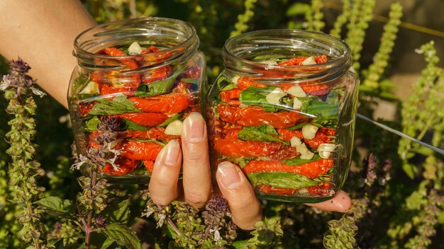 mulher faz preparativos para tomates secos de inverno, alho picado e manjericão fresco são colocados em frascos