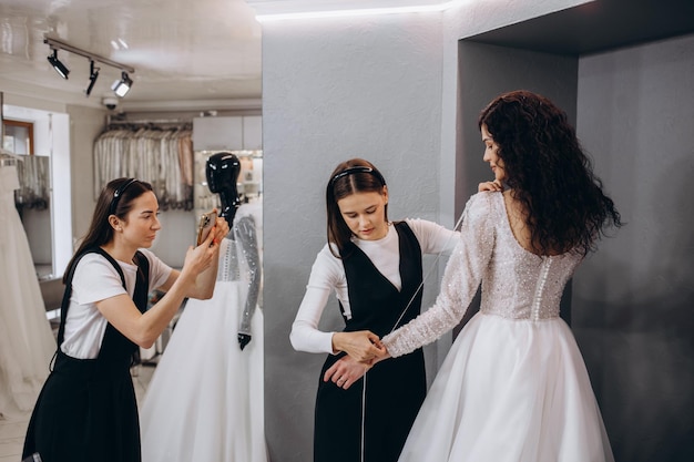 Mulher fazendo ajuste ao vestido de noiva no estúdio de designer de moda Noiva vestindo seu vestido de noiva com designer de vestido feminino fazendo ajustes finais no vestido