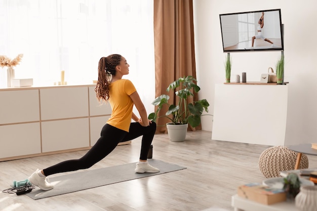 Foto mulher fazendo alongamento para frente assistindo treino na televisão dentro de casa