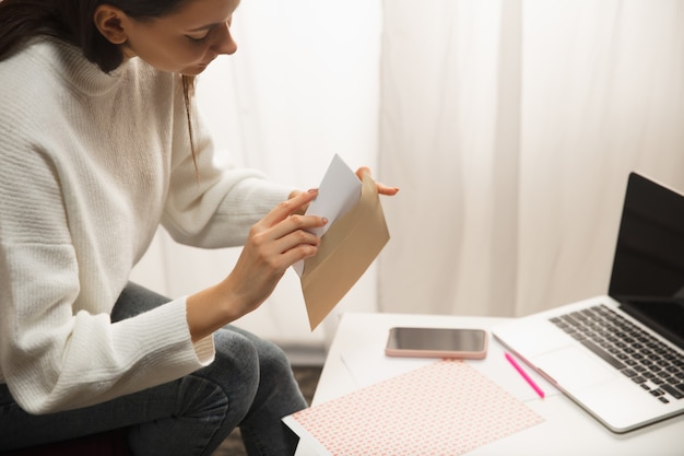 Mulher fazendo cartão de felicitações para o ano novo e o Natal de 2021 para amigos ou família, reserva de sucata, faça você mesmo. Escrevendo uma carta com os melhores votos, desenhe seu cartão caseiro. Férias, celebração.