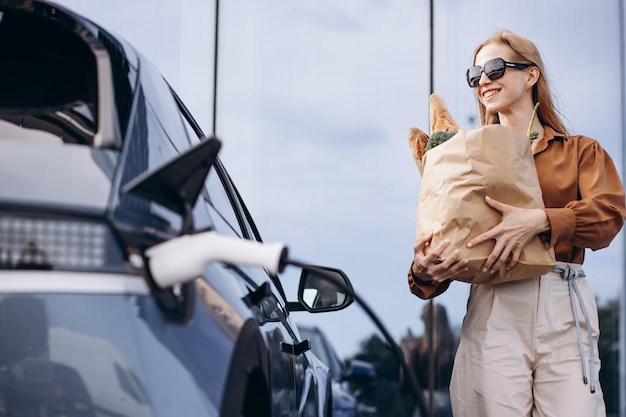 Mulher fazendo compras enquanto carrega carro elétrico