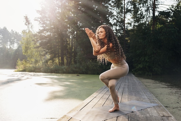 Mulher fazendo exercício garudasana pose de águia em uma ponte de madeira em uma manhã de verão no parque