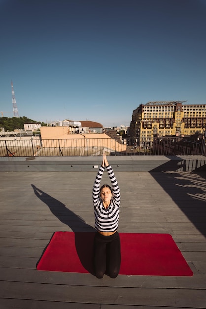 Mulher fazendo exercícios de ioga no telhado da casa no início da manhã