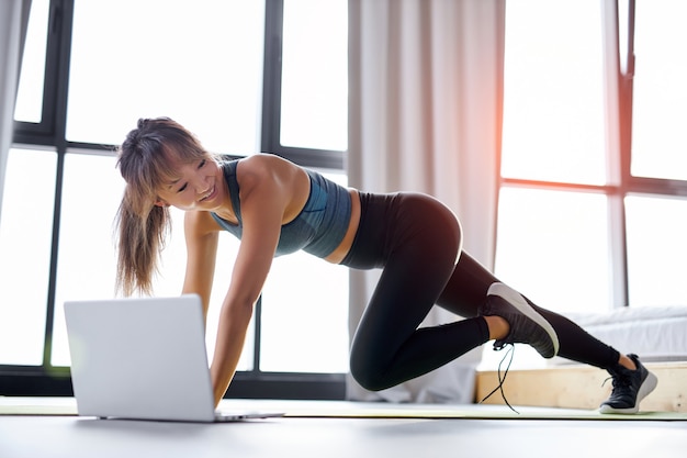 Mulher fazendo exercícios esportivos online em casa, o auto-isolamento é benéfico, entretenimento e educação na Internet. conceito de estilo de vida saudável.