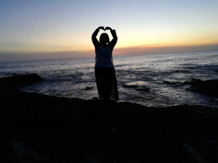 Foto mulher fazendo gestos enquanto está de pé na costa contra o mar durante o pôr do sol