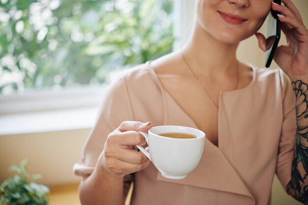 Mulher fazendo pausa, falando ao telefone e tomando café