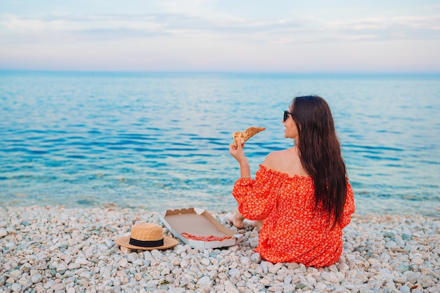 Mulher fazendo piquenique com pizza na praia