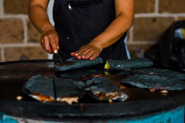 Mulher fazendo quesadillas mexicanas com milho azul e flor de abóbora.