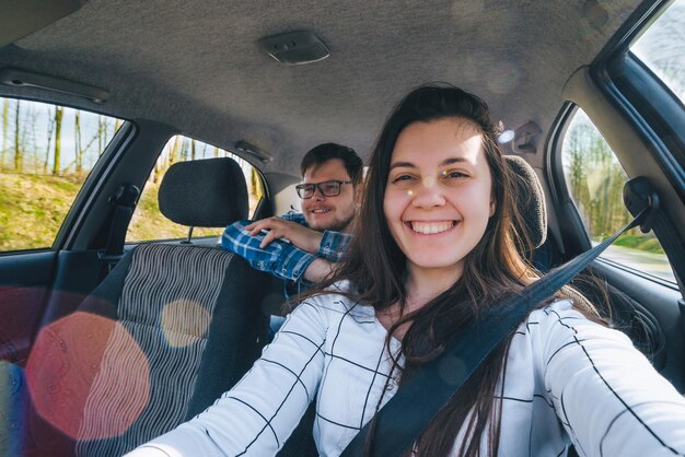 Mulher fazendo selfie enquanto dirigia o carro com o homem escorregando nos bancos traseiros. conceito de viagem de carro