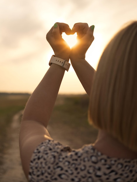 Foto mulher fazendo símbolo de coração com as mãos ao pôr do sol ao ar livre