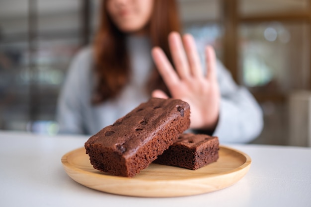 Mulher fazendo sinal com a mão para recusar um bolo de brownie em um prato de madeira