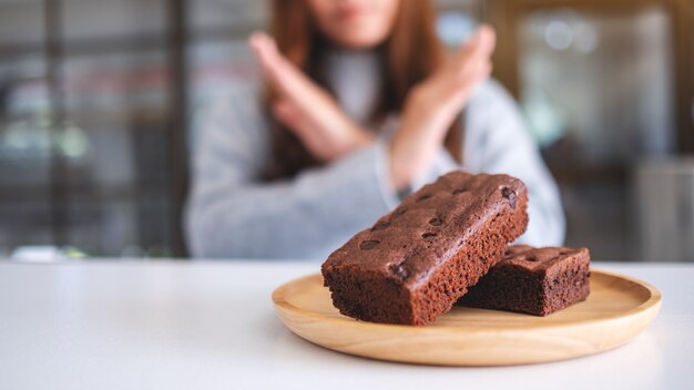 Mulher fazendo sinal cruzado de braços para recusar um bolo de brownie em um prato de madeira