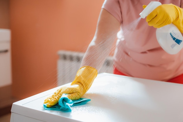 Mulher fazendo tarefas no banheiro em casa, pia e torneira de limpeza de superfícies com esponja de espuma de detergente em spray