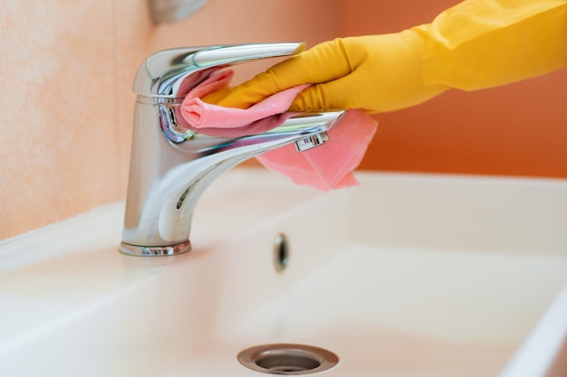 Mulher fazendo tarefas no banheiro em casa, pia e torneira de limpeza de superfícies com esponja de espuma de detergente em spray