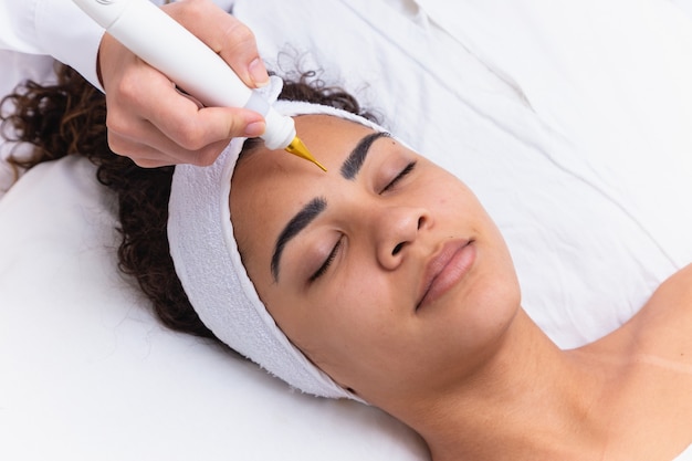 Mulher fazendo tratamento facial com jato de plasma em clínica de beleza.