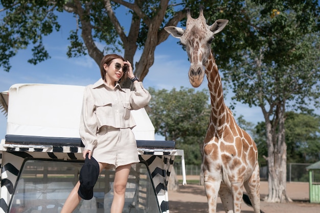 Mulher fazendo um passeio de ônibus, alimentando e brincando com a girafa no zoológico safari parque aberto.