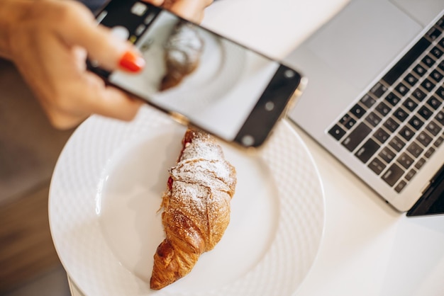 Mulher fazendo uma foto de croissant em um café