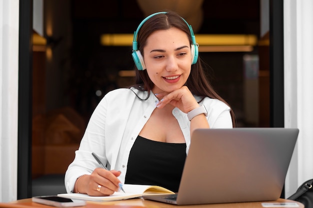 Mulher fazendo videochamada em um laptop em um café e fazendo anotações