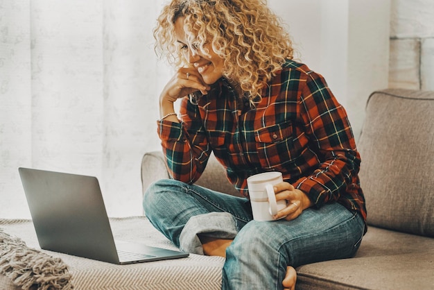 Mulher fazendo videoconferência confortavelmente sentada no sofá em casa em atividade de lazer de tecnologia Mulher usando computador no sofá Pessoas on-line modernas desfrutam de conexão com a internet e sorriem