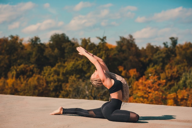 Mulher fazendo yoga no telhado de um arranha-céu na cidade grande.