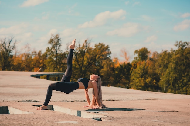 Mulher fazendo yoga no telhado de um arranha-céu na cidade grande.