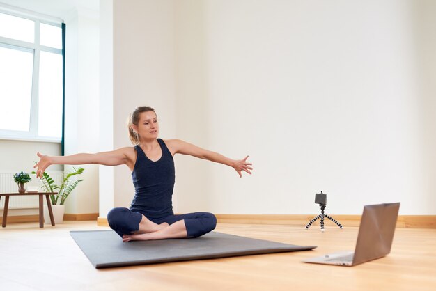 Mulher fazendo yoga online. Computador e câmera em sua sala de estar. Estilo de vida saudável e conceitos de trabalho à distância