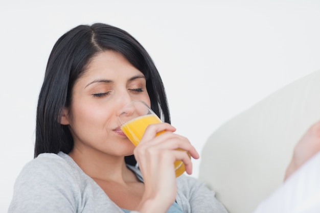 Mulher fechando os olhos enquanto toma um copo de suco de laranja