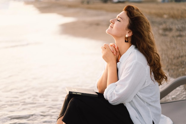 Foto mulher fechou os olhos orando em um mar durante o belo pôr do sol