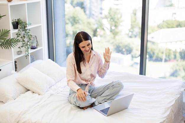 Mulher feliz acenando olá enquanto fala por videochamada usando laptop moderno