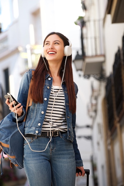 Mulher feliz andando com fones de ouvido e bagagem fora