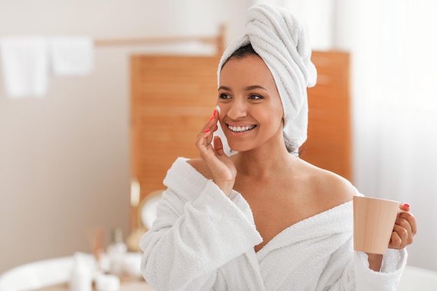 Mulher feliz aplicando hidratante na pele do rosto hidratante no banheiro