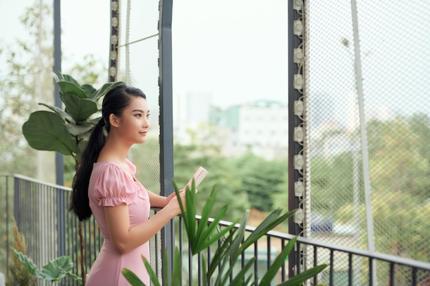 Mulher feliz atraente em roupas casuais lendo livro no terraço