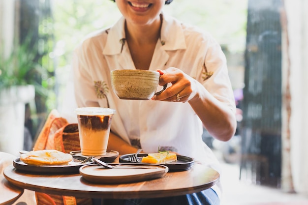 Foto mulher feliz bebe café e come bolo no café