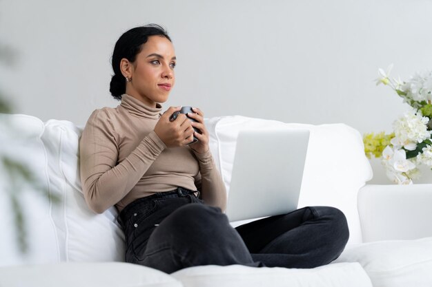 Mulher feliz bebendo café em um sofá em casa para descanso e relaxamento cruciais