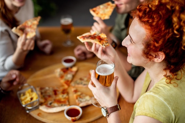 Mulher feliz bebendo cerveja e comendo pizza com amigos em um pub