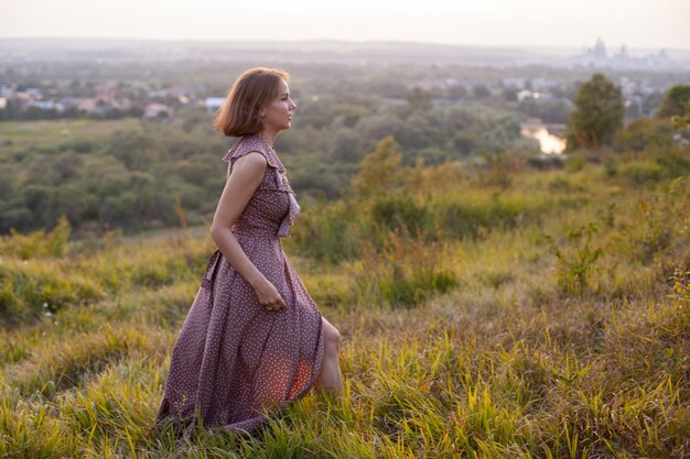 Mulher feliz caminha ao pôr do sol em uma colina com vista para o rio