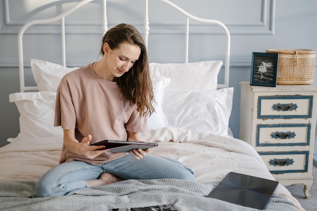 Mulher feliz casual com fones de ouvido trabalhando em um laptop remotamente de casa na cama