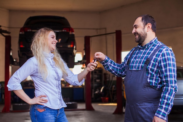 Mulher feliz cliente satisfeita recebendo as chaves do carro da automecânica depois que seu carro foi reparado Cliente homem e mulher e trabalhador de reparação de automóveis no serviço automático