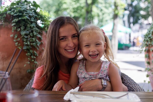 Mulher feliz com a garotinha loira em uma mesa na esplanada do refeitório.