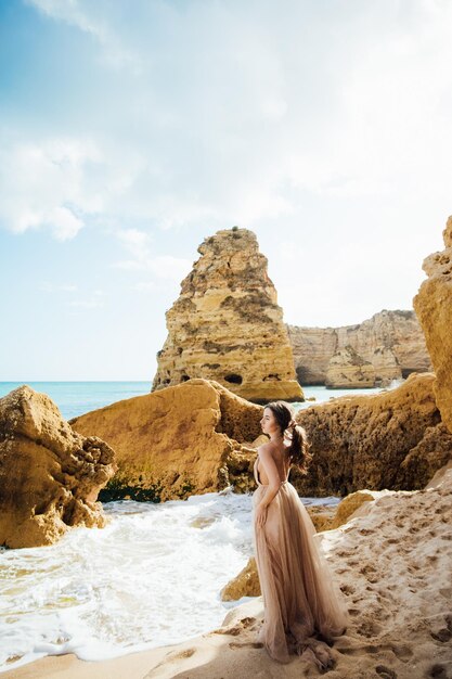 mulher feliz com as costas em um vestido amarelo em pé na praia e o mar ao pôr do sol