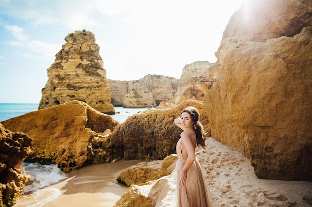 mulher feliz com as costas em um vestido amarelo em pé na praia e o mar ao pôr do sol