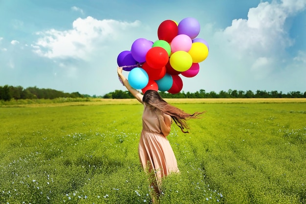 Mulher feliz com balões coloridos em campo no fundo do céu azul