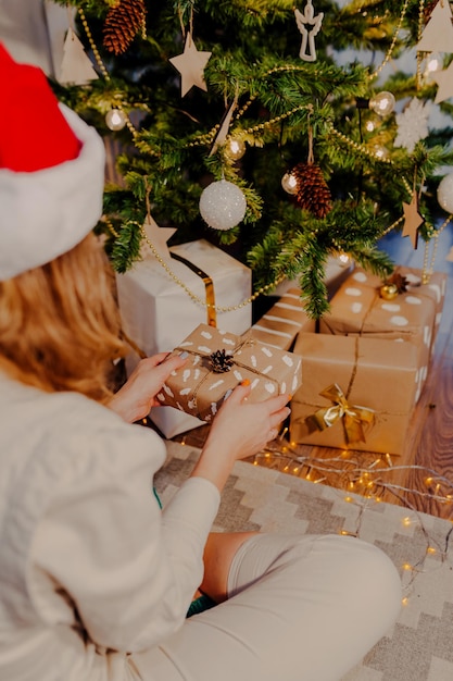 Mulher feliz com chapéu de Papai Noel com presente de Natal nas mãos. Mulher sentada debaixo da árvore de Natal.