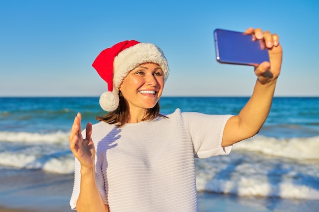 Mulher feliz com chapéu de papai noel na praia