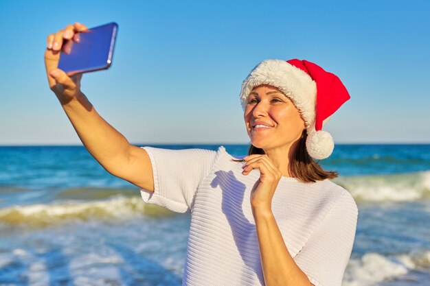 mulher feliz com chapéu de Papai Noel na praia