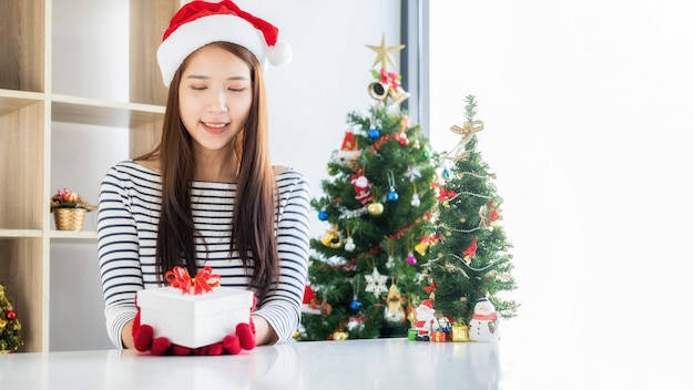 Mulher feliz com chapéu de Papai Noel segurando uma bela caixa de presente na mesa branca. Feliz natal e feliz ano novo.