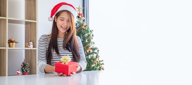 Mulher feliz com chapéu de Papai Noel segurando uma bela caixa de presente na mesa branca. Feliz natal e feliz ano novo.